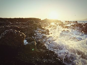 Sea waves splashing against clear sky during sunset