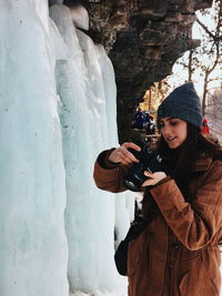 Young woman photographing with camera standing in snow