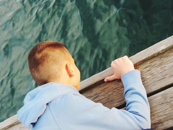 High angle view of boy looking at lake while leaning on pier