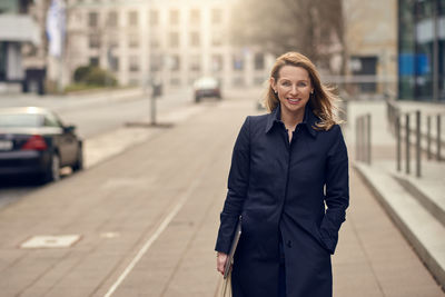 Portrait of smiling woman standing on sidewalk in city