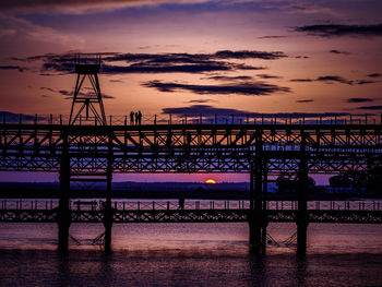 Silhouette bridge over sea against sky during sunset