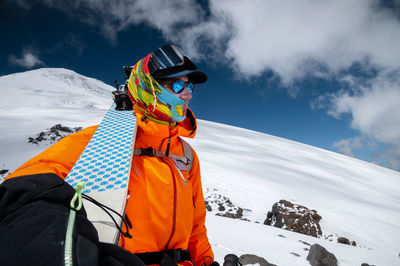 Wide angle shot young tall professional skier holds his skis while standing high in the mountains 