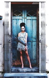 Portrait of smiling young woman standing against door
