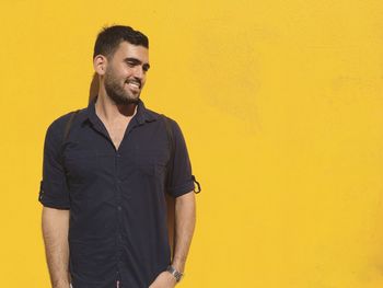 Portrait of smiling young man standing against yellow wall