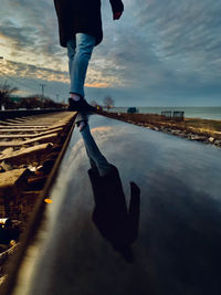 Low section of man standing on railroad track against sky