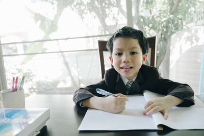 Portrait of boy holding pen over paper while sitting on table