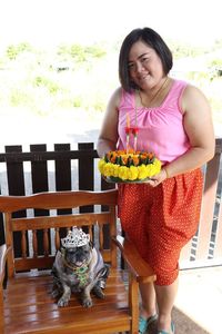 Portrait of smiling woman with dog holding cake while outdoors