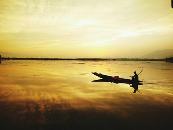 Silhouette person in boat on sea against sky during sunset