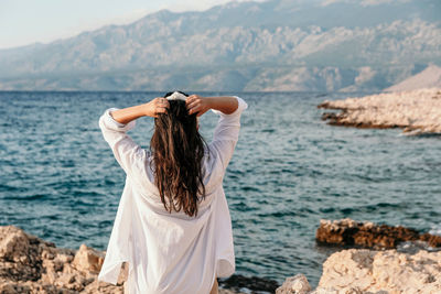 Rear view of woman standing on rock by sea