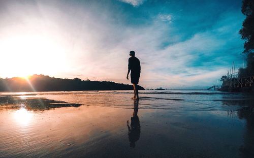 Silhouette man standing at beach against sky during sunset