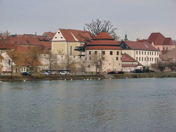 Houses by river and buildings in town against sky