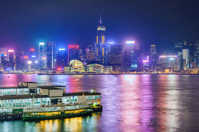 Illuminated buildings by river against sky in city at night