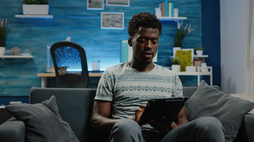 Young man using digital tablet white sitting on sofa at home