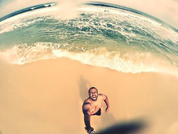 High angle fish-eye lens shot of shirtless man screaming while standing at beach