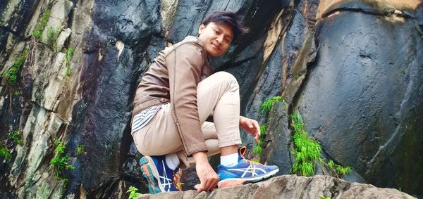 Woman sitting on rock against wall