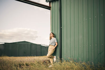 Woman standing with hand in pocket while leaning on corrugated wall