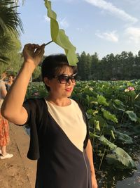 Woman wearing sunglasses holding leaf while standing outdoors