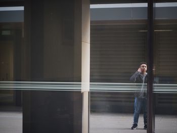 Full length of young man talking on phone seen through glass window