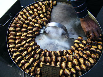 Cropped image of hand arranging roasted chestnuts on container at stall