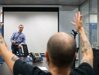 Businessman standing against projection screen while coworker sitting at table in office