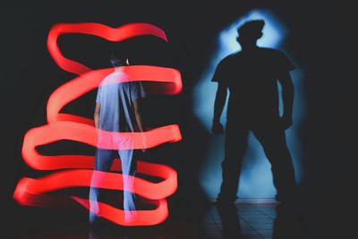 Rear view of silhouette man standing against illuminated background