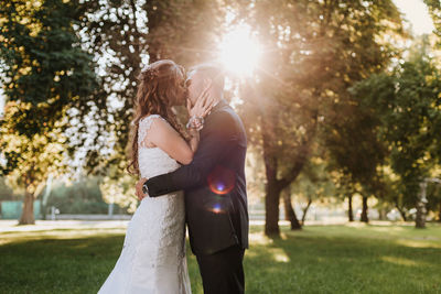 Side view of couple kissing while standing against trees