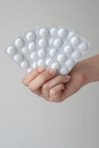 Cropped hand of person holding pills against white background