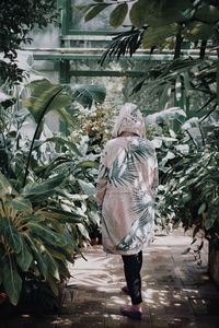 Rear view of mid adult woman walking by plants in greenhouse