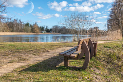 Empty bench in park by lake against sky