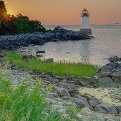 Lighthouse by sea against sky during sunset