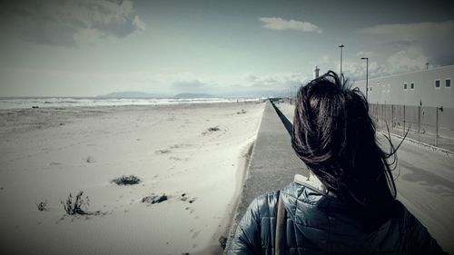 Rear view of woman standing on beach against sky