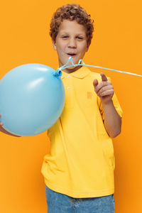 Portrait of young woman with balloons while standing against yellow background