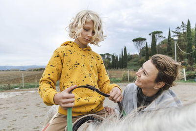 Happy mother looking at boy sitting on horse