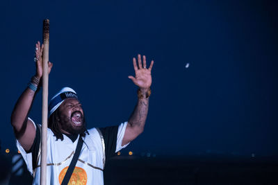 Young man screaming while standing by pole against sky at night