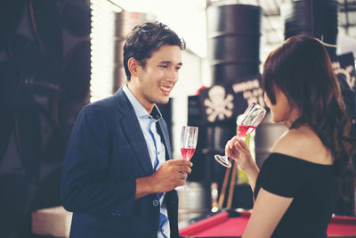 Smiling couple toasting red wineglasses while standing in bar