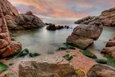 Rocks on sea shore against sky during sunset