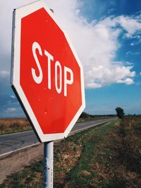 Stop sign board by street against sky