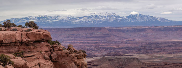 Rugged red sandstone rock formations tower above the eroded landscape snow capped mountains behind