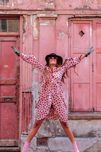 Model in pink polka dot dress and gloves with black hat in london jumping of happiness 