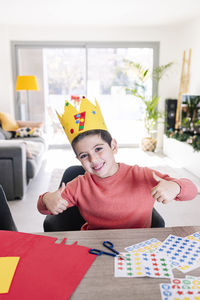 Portrait of boy wearing crown sitting by table at home
