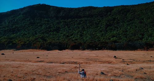 Rear view of man sitting on field by mountain