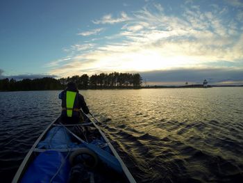 Rear view of man sailing on boat in river against sky during sunset