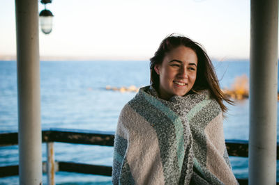 Smiling young woman standing on pier over sea