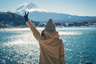 Rear view of woman showing peace sign against mountain