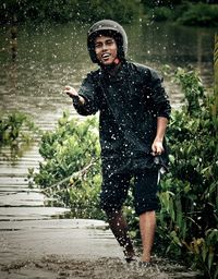 Portrait of man in raincoat standing at river during rainy season