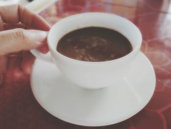 Close-up of hand holding coffee cup on table
