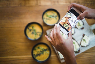 Hands of female blogger photographing pumpkin soup and crispbread through smart phone at creative office