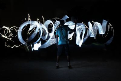 Rear view of man standing on illuminated road at night