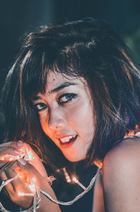 Close-up portrait of young woman holding illuminated string light