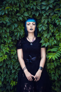 Beautiful goth girl with bright blue hair standing in the green ivy. on the eve of halloween